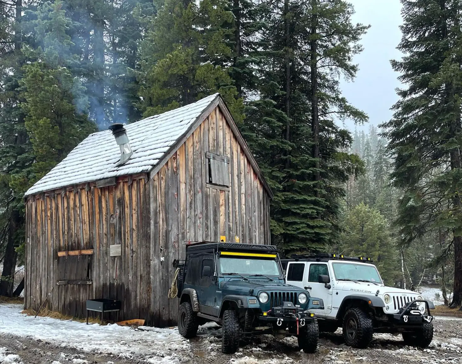 Two off-road vehicles parked beside a wooden cabin in a snowy forest