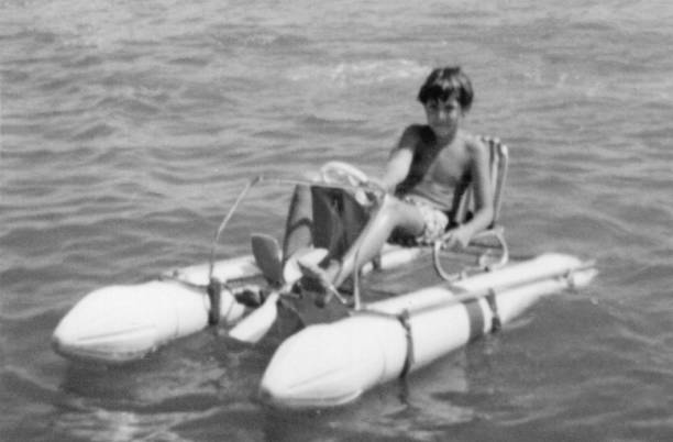 Vintage black and white photo of a boy on a pedal-powered catamaran