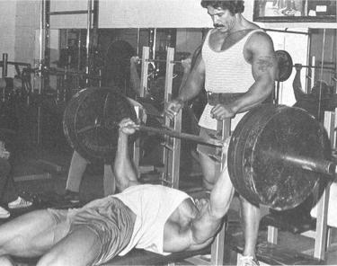 Arnold Schwarzenegger performing a bench press in a gym